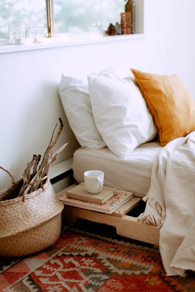 cozy bedding with orange pillow and mug on books