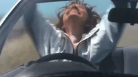 Woman waving her hands in happiness while driving a car.