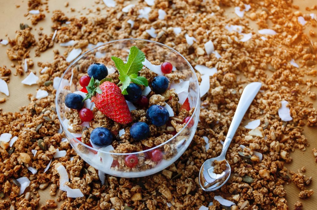 Mix of granola, nuts, blueberries and strawberries in a bowl. With a spoon and granola on the table.