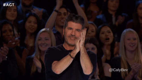 Simon Cowell in America's Got Talent clapping and giving two thumbs up.