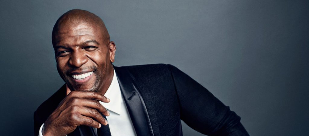 Terry Crews smiling against a grey background.