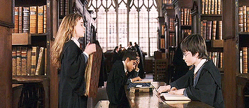 Hermione Granger slamming a thick book on the desk in front of Harry Potter in the library.