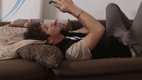 Man lying down on couch dropping his phone on his face.
