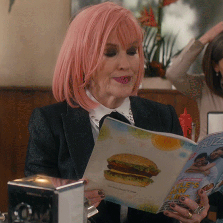 Woman with pink hair looking at a menu, pausing and giving a hesitant look to the side.