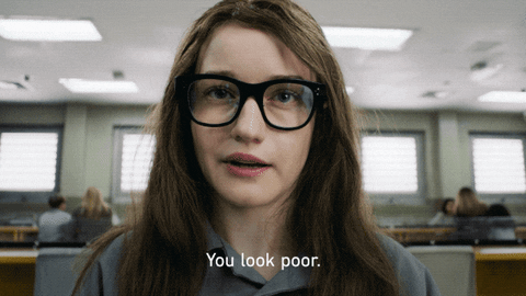 Anna from the series "Inventing Anna" is wearing black glasses and saying the words "you look poor."