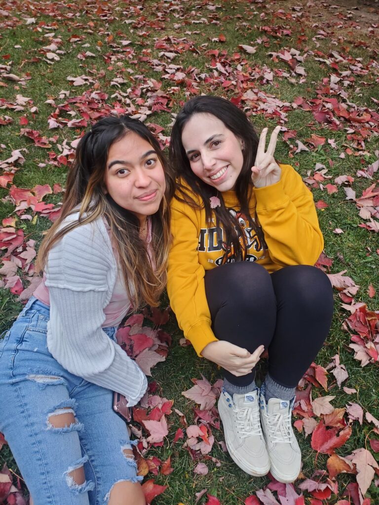 Ariely Reyes and Mariana Ferreira sitting on the grass and posing for a picture.
