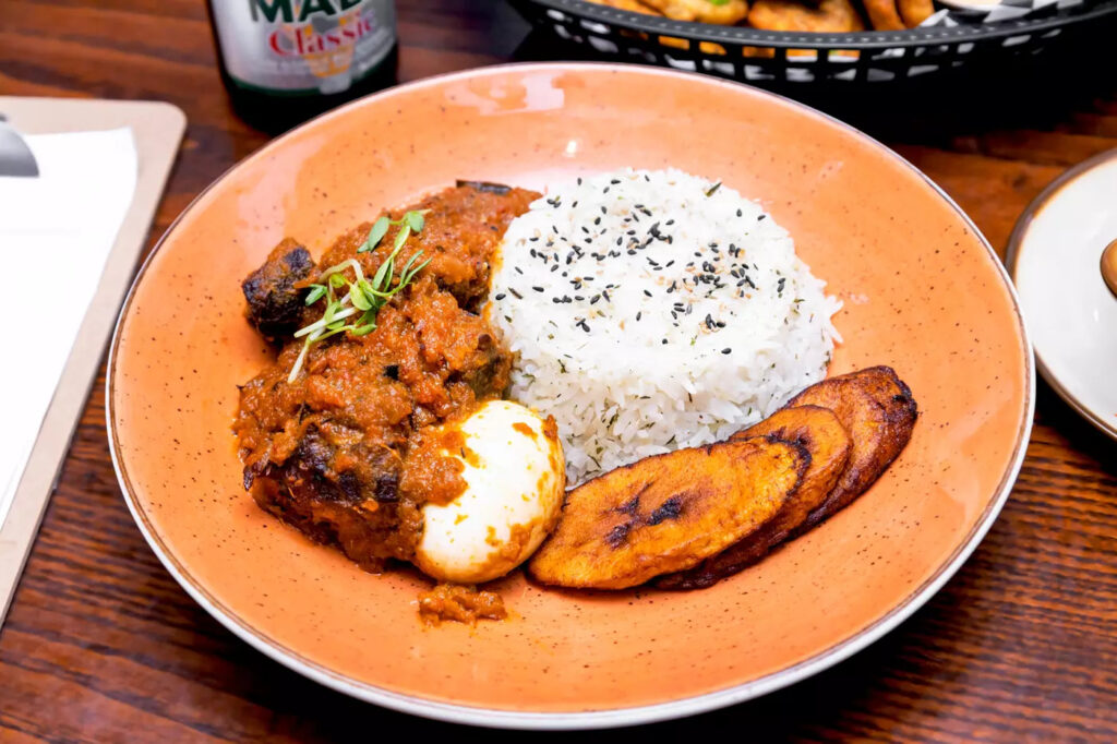 A plate of buka beef stew served with rice, hard- boiled egg and fried plantain.