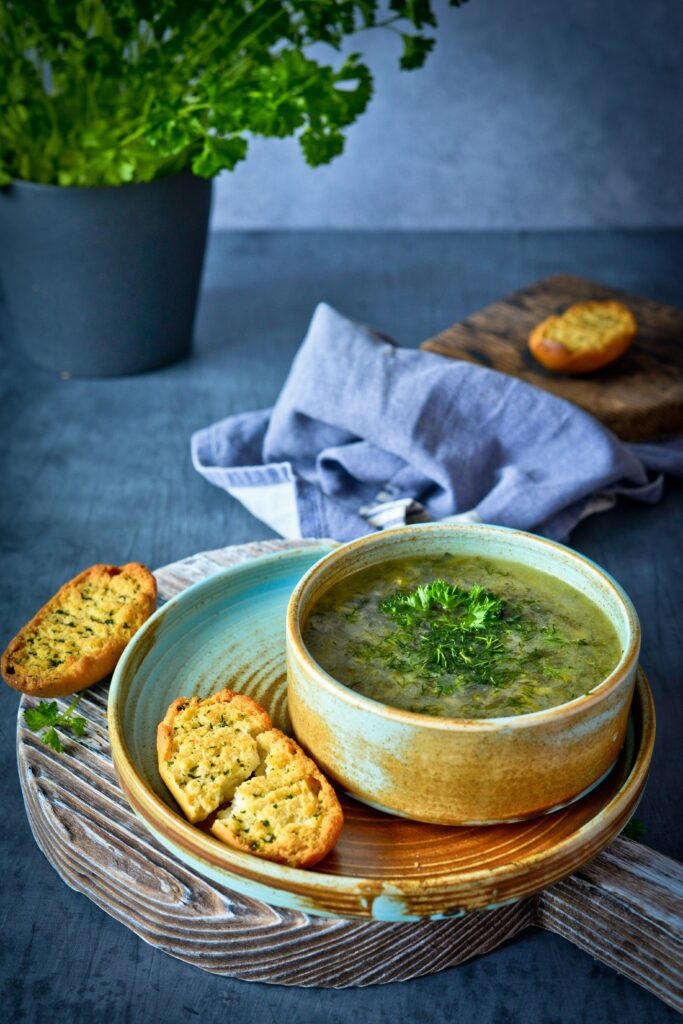 A small serving of soup is in a bowl. It is served with garlic and parsley bread.