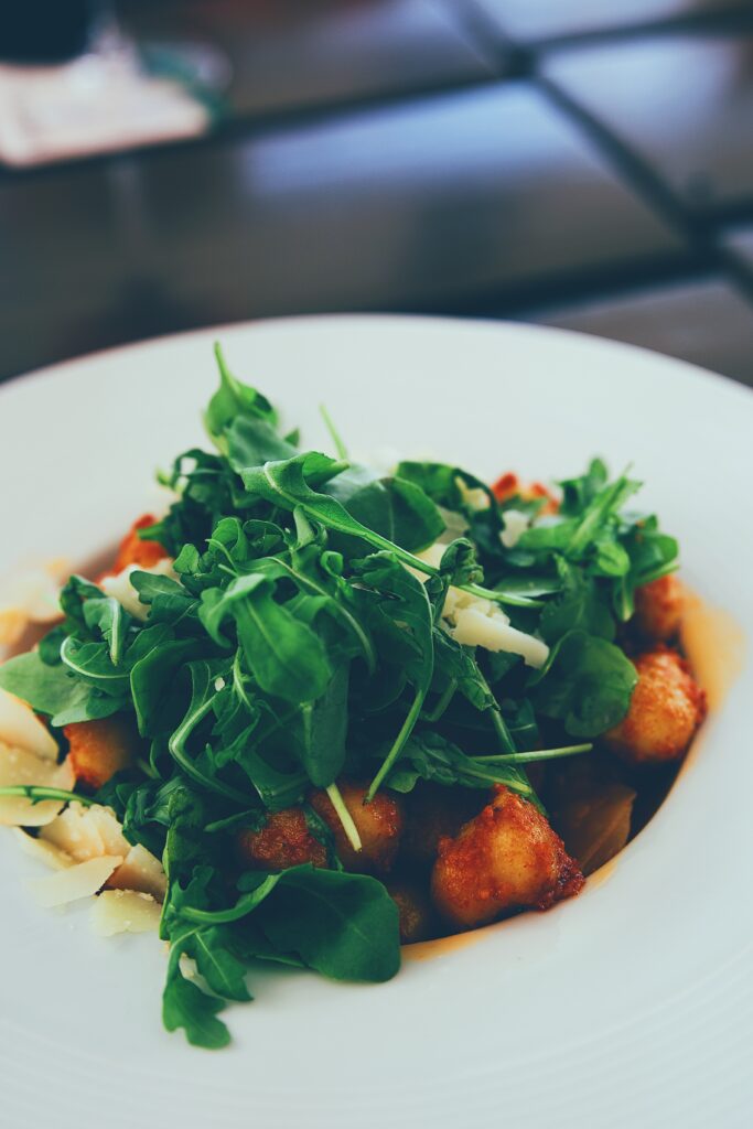 A small bowl of arugula salad made with almonds and chicken. 