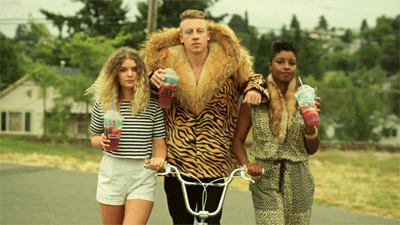 Macklemore in thrifted winter coat riding on a bike. 