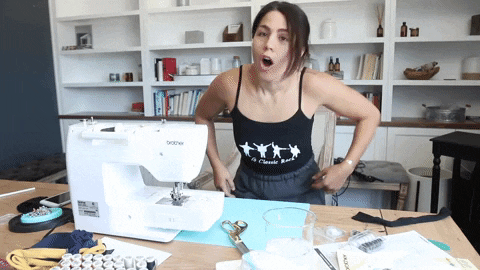A woman gesturing excitedly in front of a sewing table.