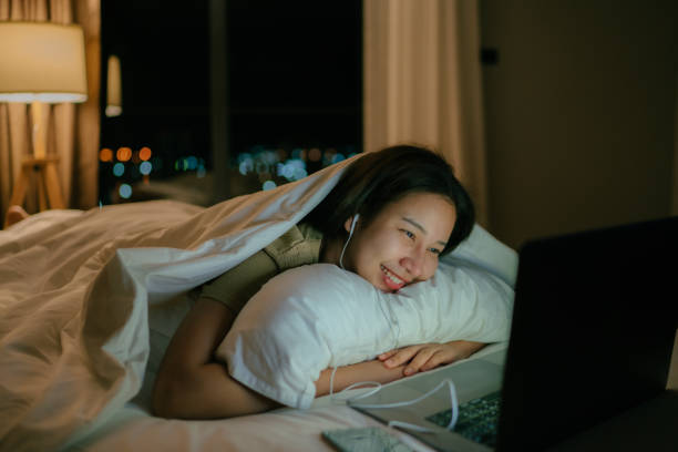 A woman under a blanket viewing her laptop.