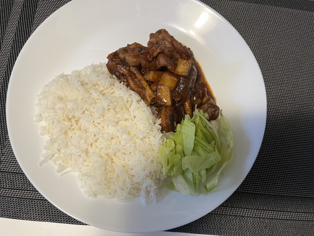 A serving of white rice, brown stew chicken and shredded lettuce.
