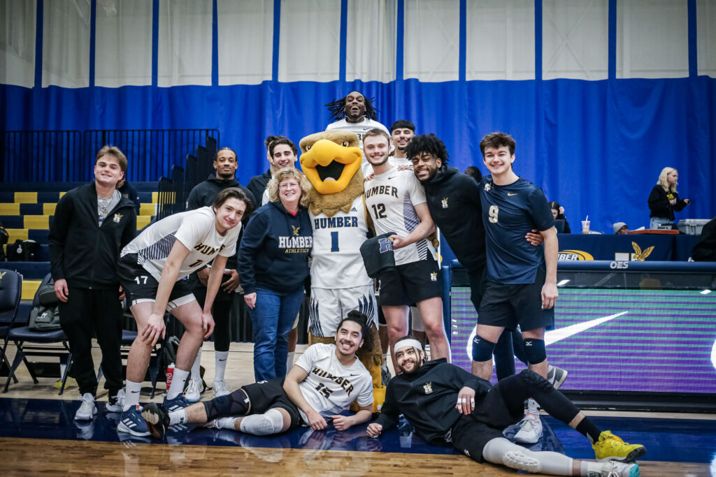 Gabriel Mendes with his teammates and Humber president Dr. Ann Marie Vaughan posing for a picture after he earned the Hawks Player of the Game award.