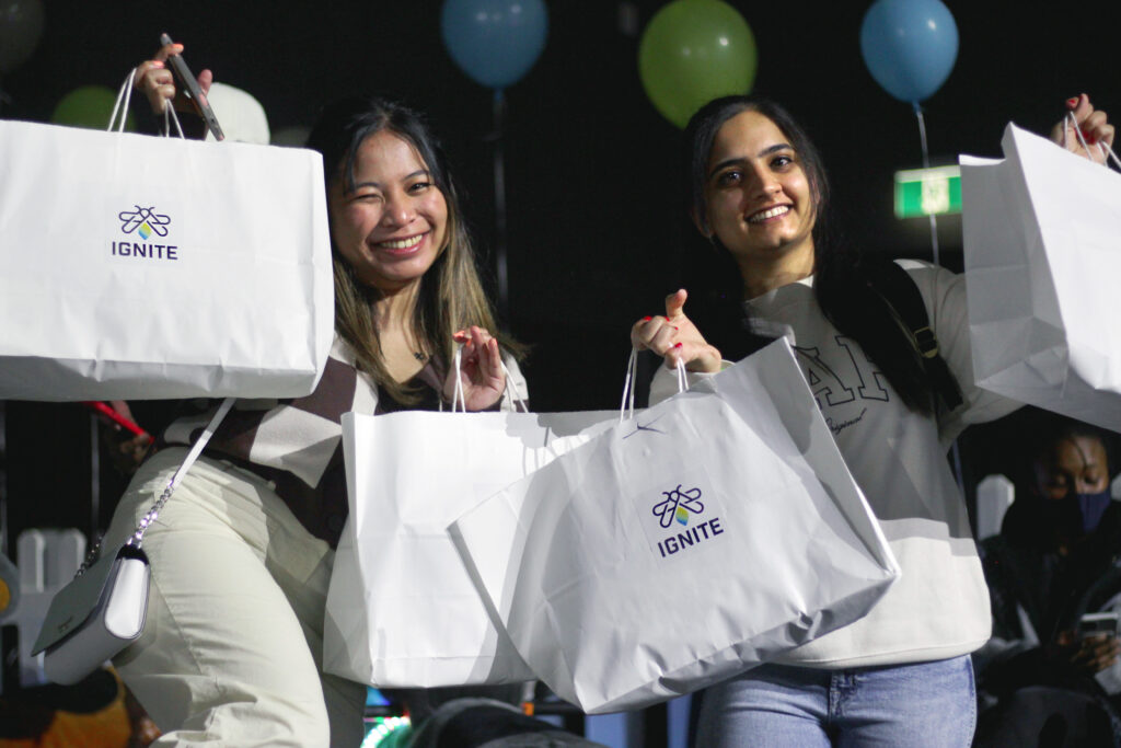 A picture of two friends smiling with IGNITE swag bags. (Hype Hall)