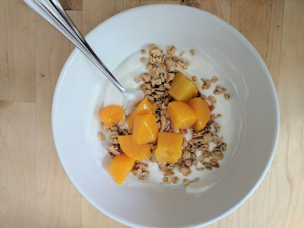 A yogurt bowl topped with peaches and granola.