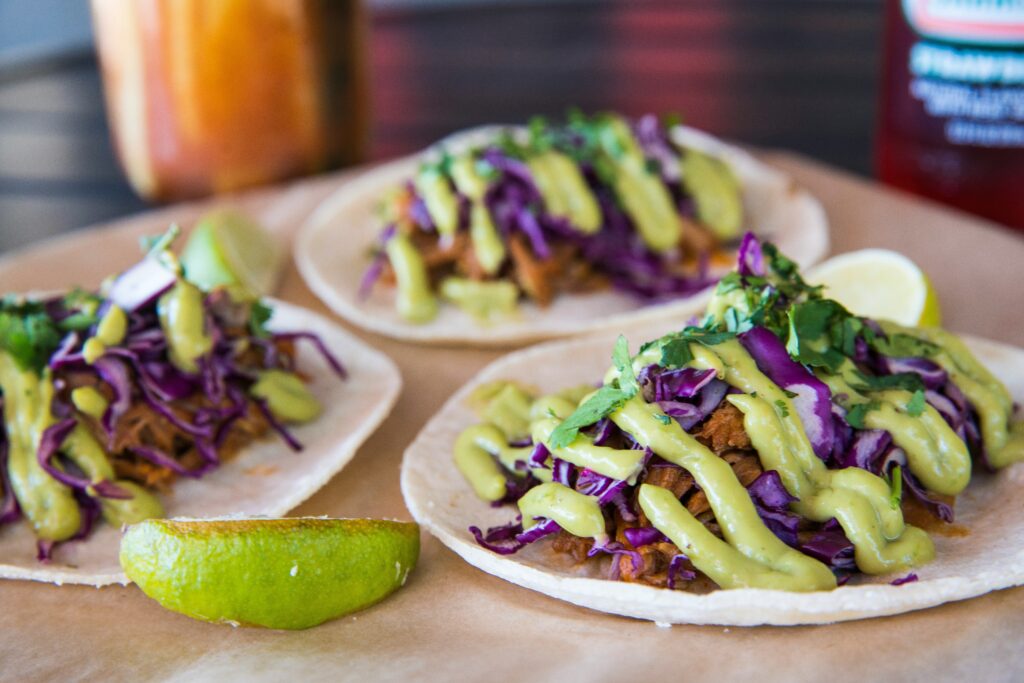 A serving of pull pork tacos, made with cabbage and garnished with lime.