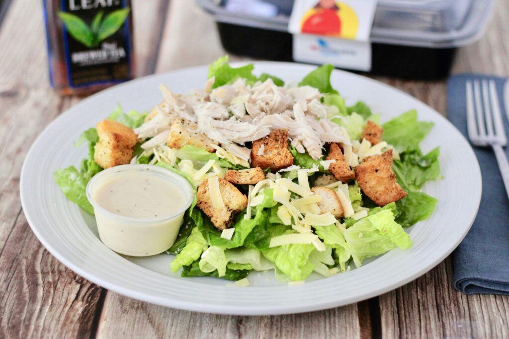 A plate of Caesar salad made with chicken, romaine lettuce, crotons and cheese. It is serving with classic Caesar dressing.
