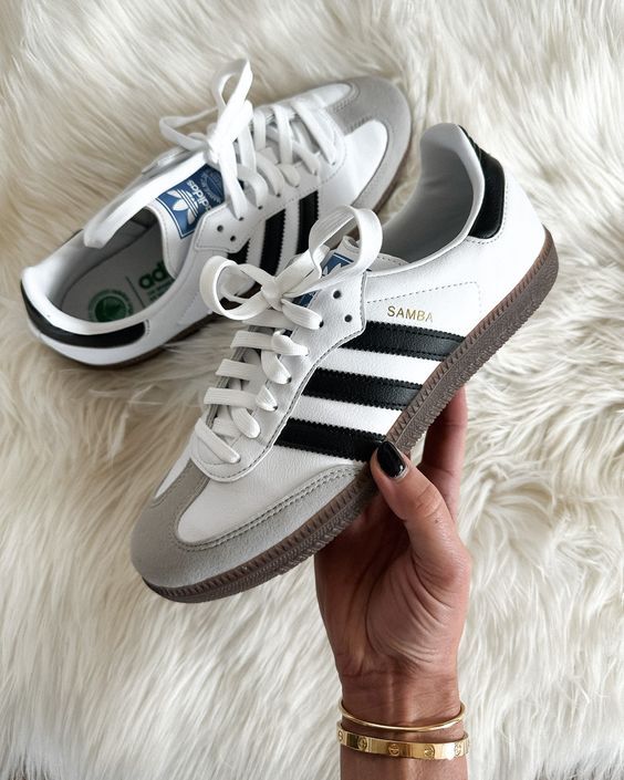 A woman is showing us a picture of her black and white Adidas Sambas.