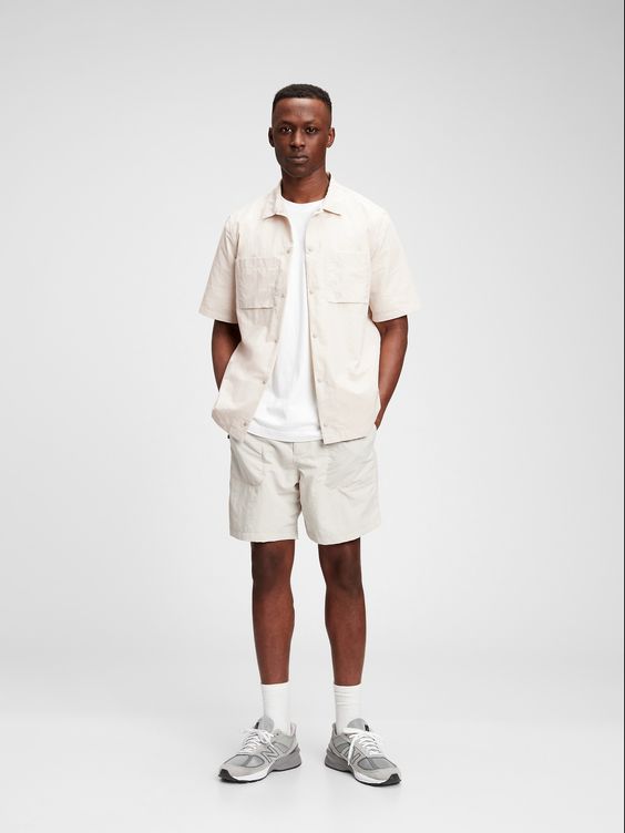 A guy is dressed in neutral shorts and a short-sleeved set. He pairs the look with his New Balance sneakers. (fashion forecast)