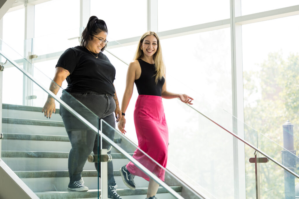 IGNITE Student Advocates Melany and Jessica walking down a staircase smiling.