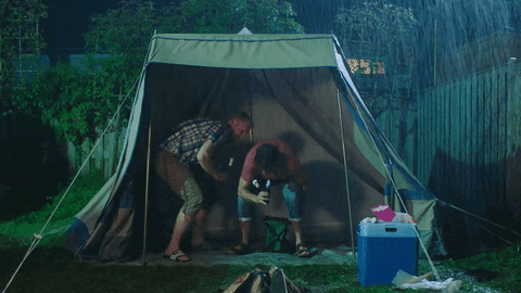 Two men sitting under a collapsing tent in the rain.