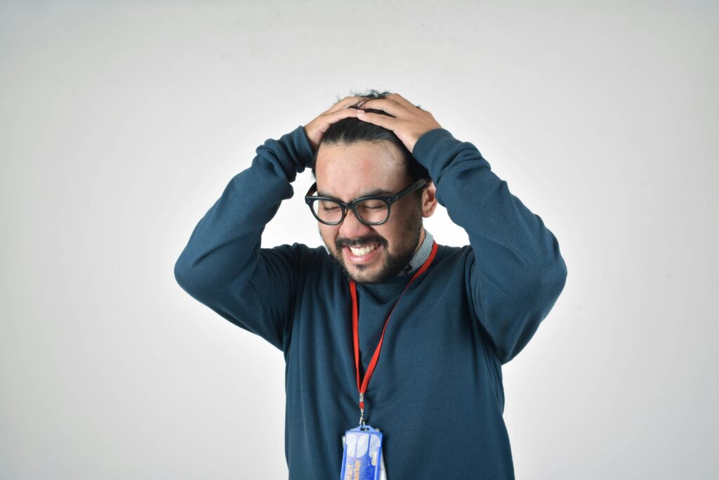 Picture of a man in a blue sweater disappointed with his hands on his head.