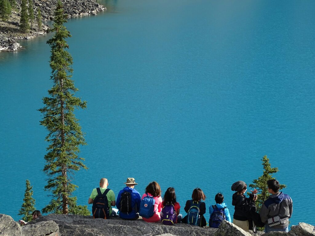 Picture of a group of travellers sitting on a rock edge facing the water relating to sustainability.