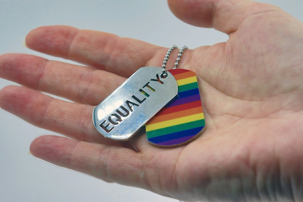 Picture of a person holding a dog tag with a Pride flag and the word “equality.”