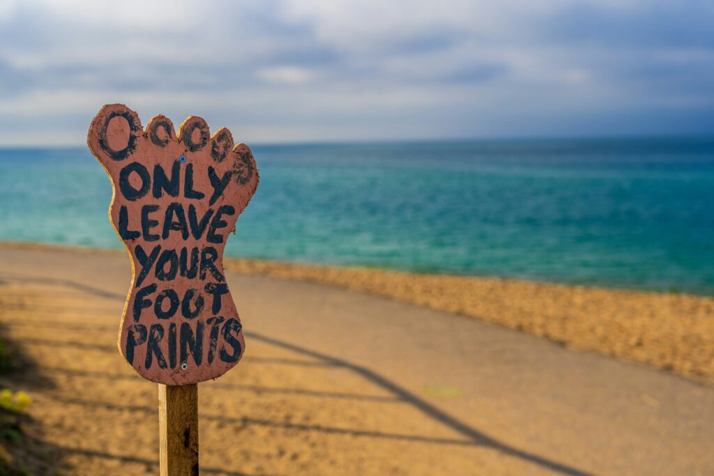 Picture of a brown wooden foot-shaped sign on a beach that reads “Only leave your footprints.”