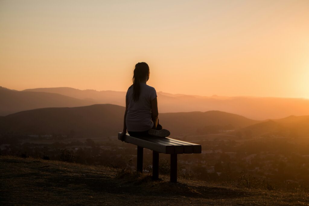 Picture of a woman sitting on a bench overlooking a mountain.