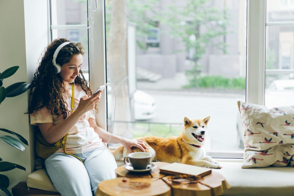 Picture of a woman listening to music sitting on a windowsill next to a dog.