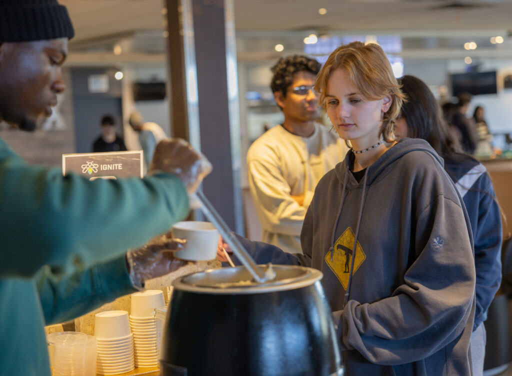 A person serving an IGNITE soup to a student.