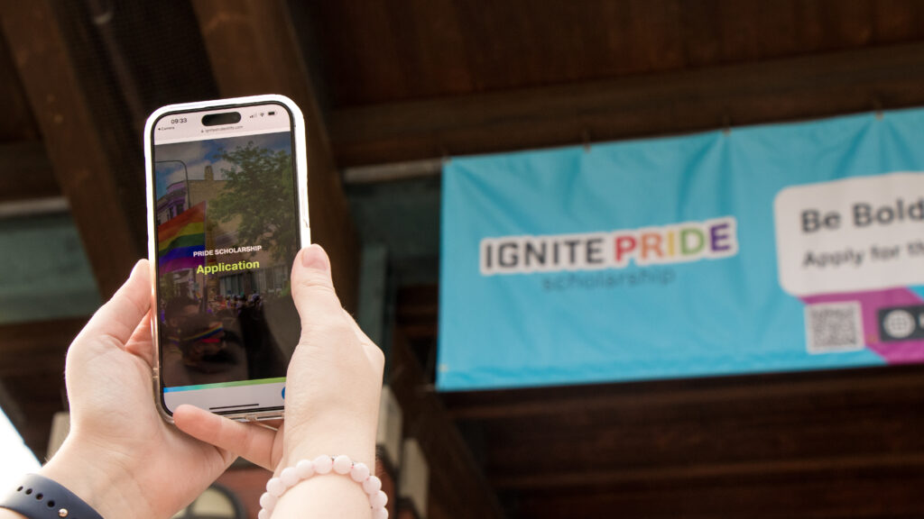 A person taking a picture of the IGNITE Pride Scholarship banner.