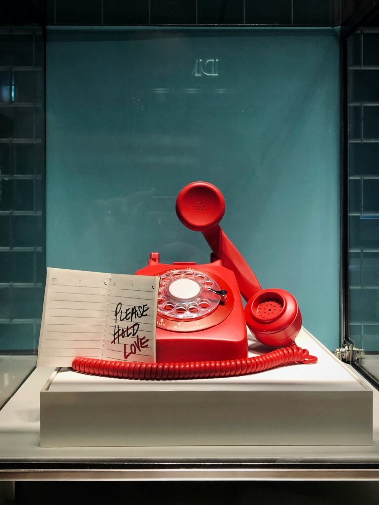 A red telephone with a message that reads “Please hold love,” with the word “hold” strikethrough.
