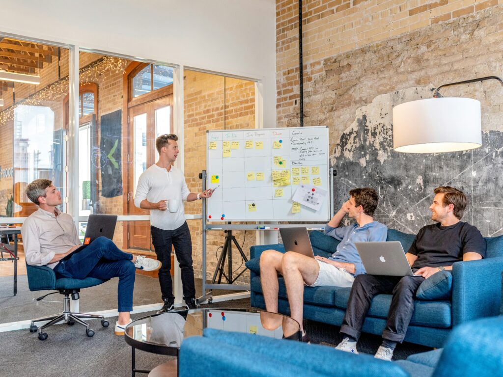 A group of people working together while a man explains using a whiteboard.