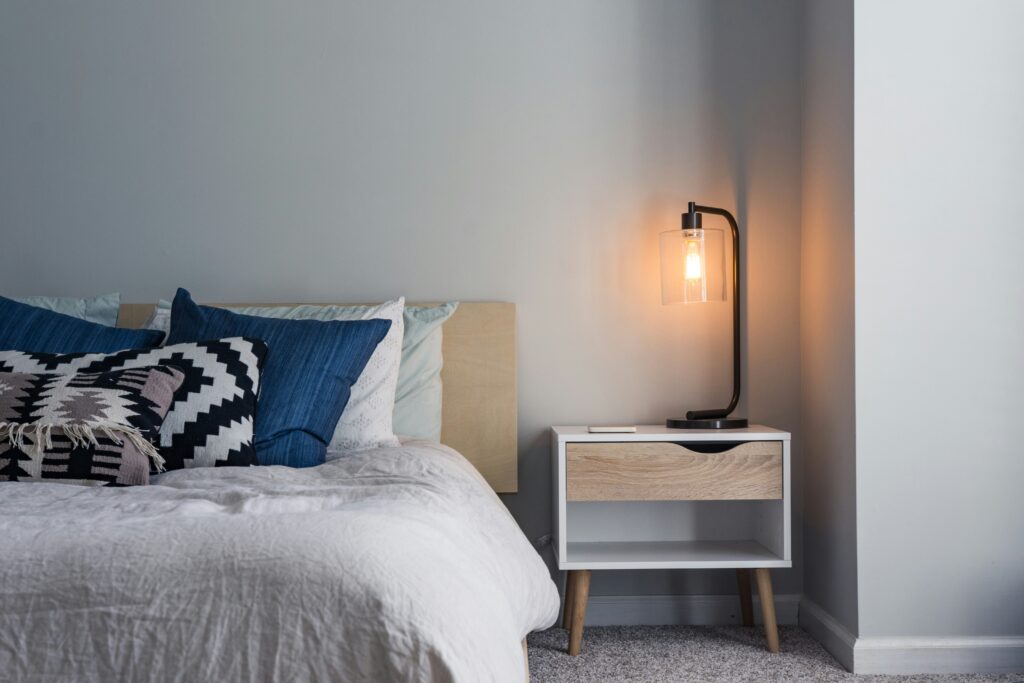 Picture of a black lamp on a nightstand beside a bed.