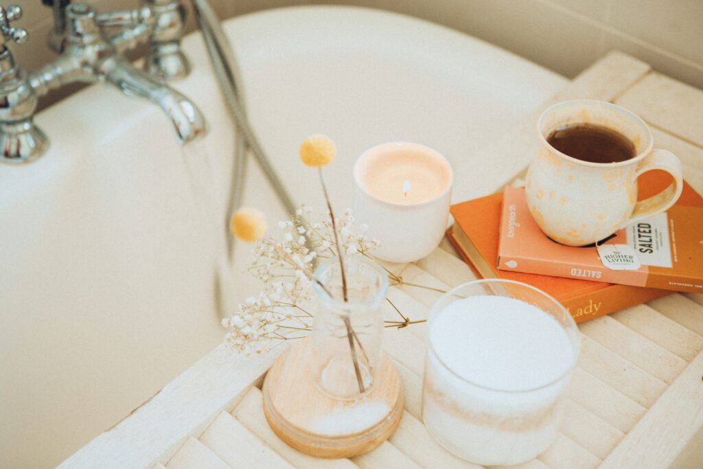 Picture of bath salts, vegan chocolate, tea and a book by a bathtub.