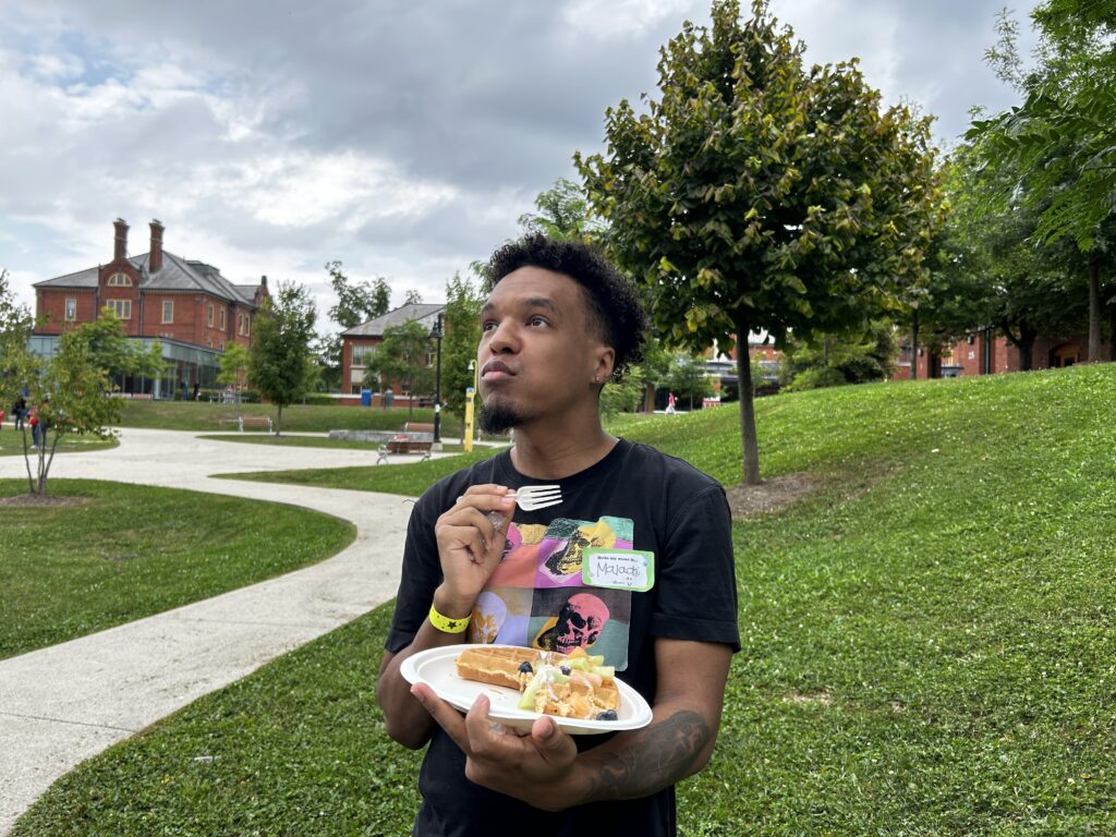 Humber student Malachi Jones holds a plate of waffles on his left hand and a fork on his right hand, as he looks up.