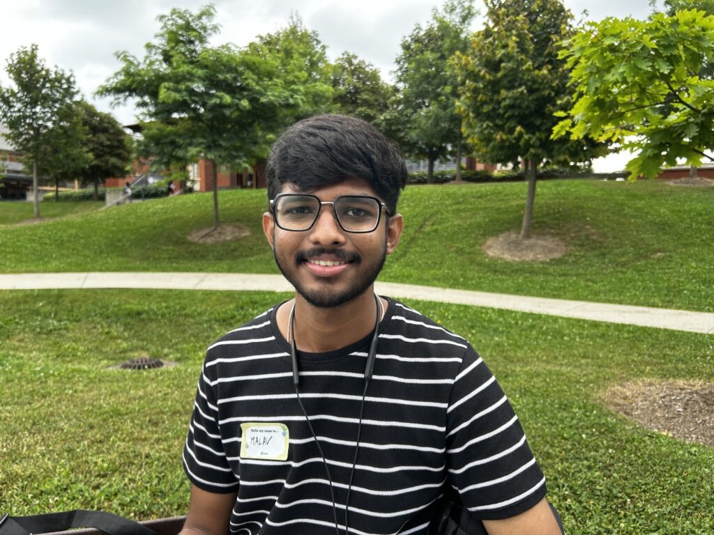 Humber student Malav Prajapati smiles as she sports a striped shirt and a pair of glasses.