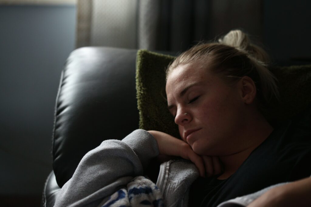 A woman sleeping on a black leather couch.