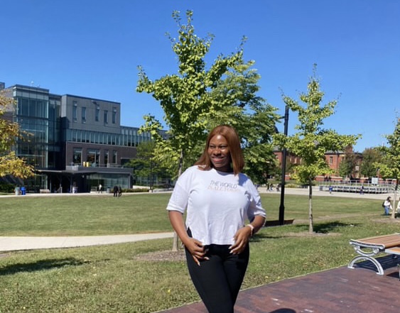 A photo of a girl standing in the middle of the Lakeshore grounds, the L building is displayed in her background.