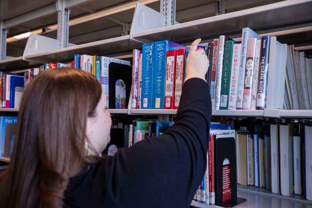 A woman is reaching for a book on the library shelf.