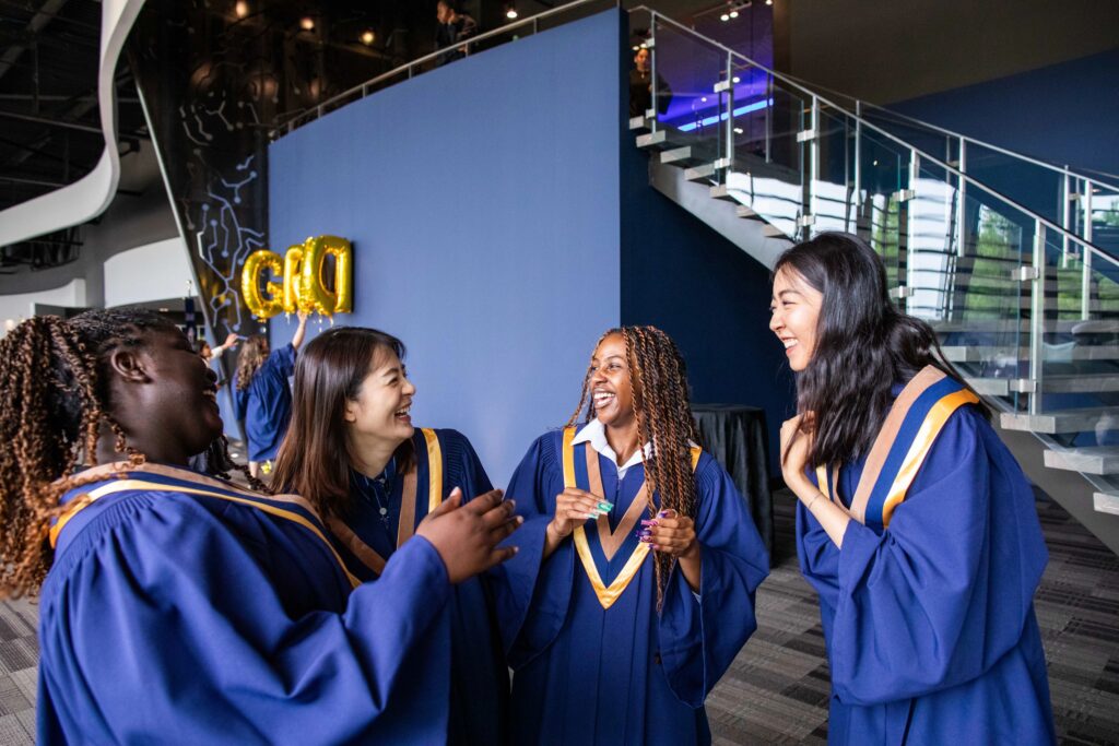 A group of women are standing together and laughing while wearing graduation gowns. 