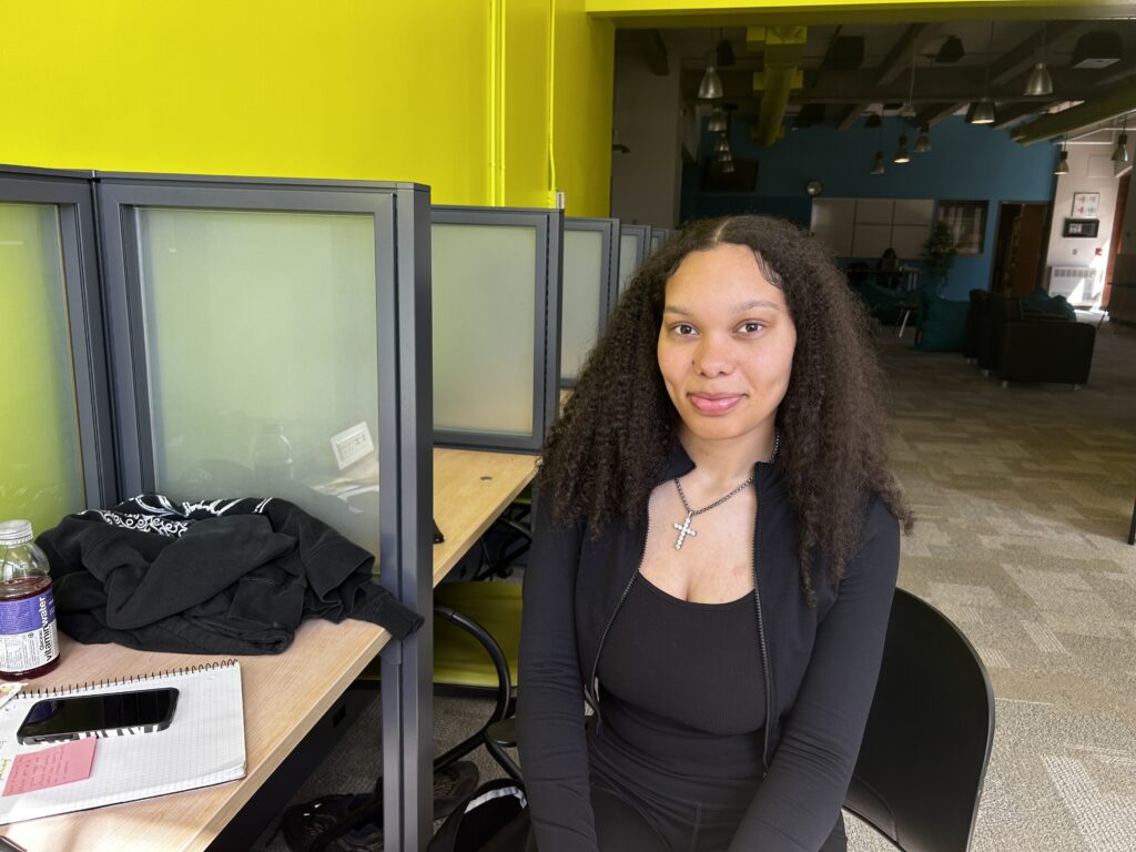 A girl sits in one of the cubicle chair at the IGNITE Zen Zone. She is smiling at the camera.