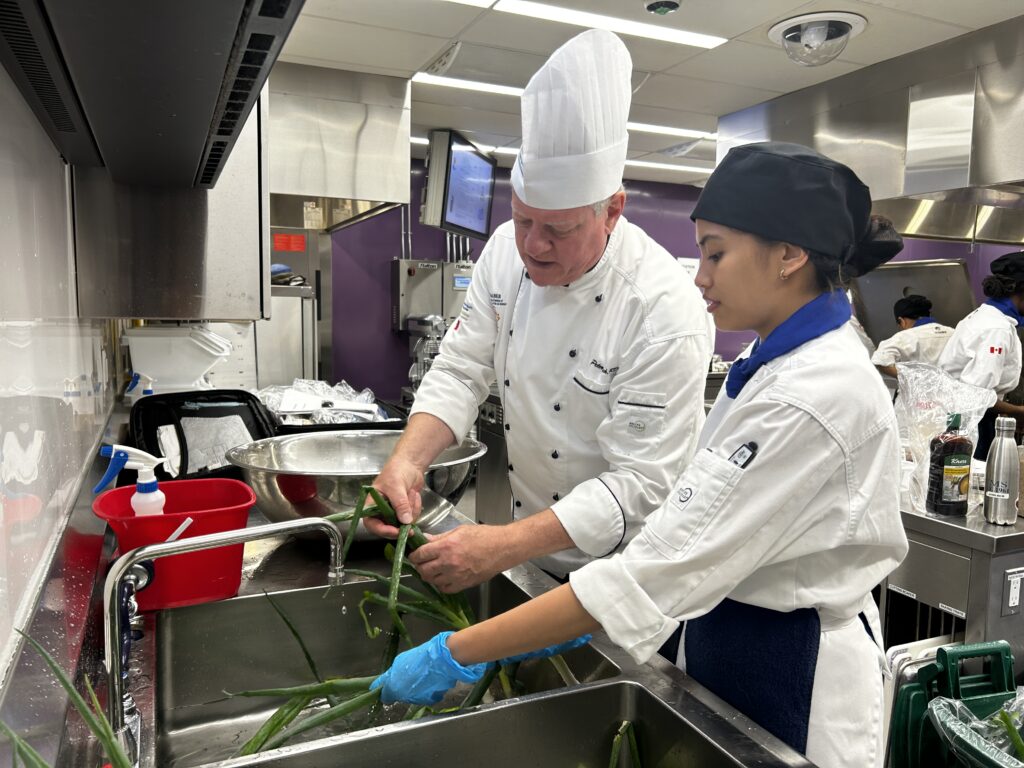 Chef Peter Rick shows a nutrionist student how to properly clean the leaf of green onions.