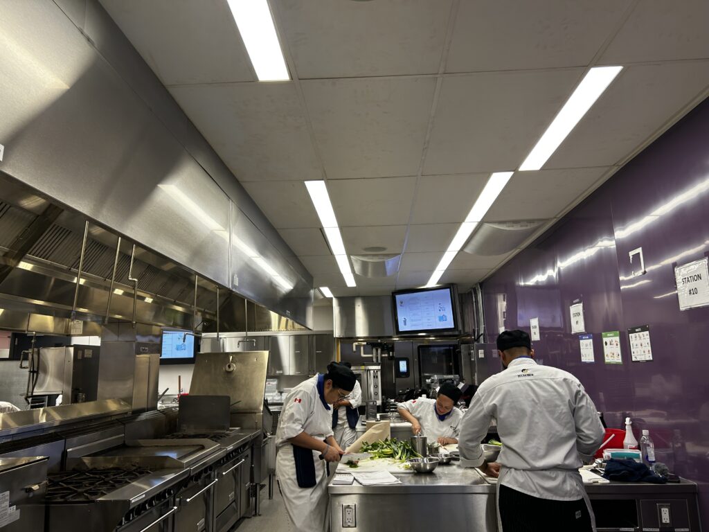 Nutrionist students chopping vegetables in an industrial kitchen.