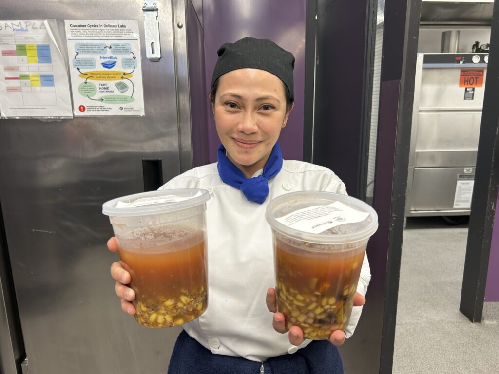 A nutrionist student holds out her hands as she hold two containers filled with tomato vegetable soup.