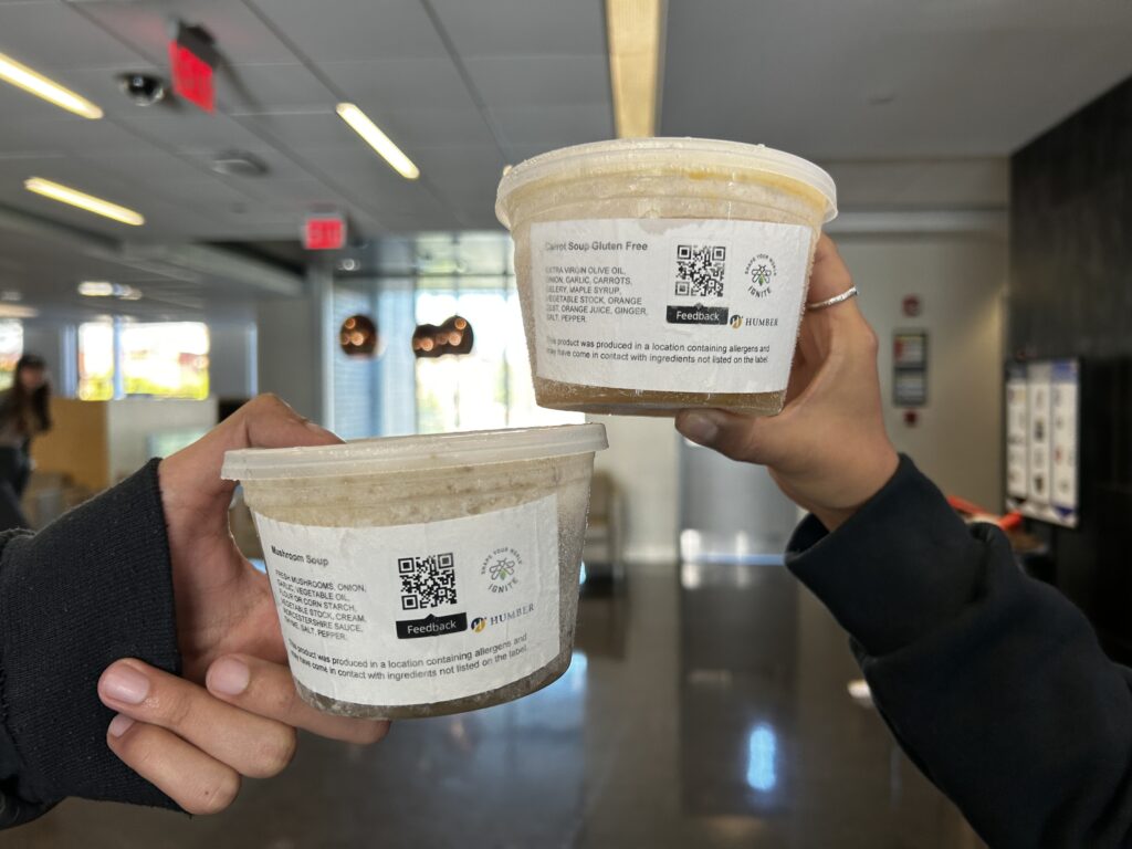 A close up shot of 2 hands holding out tubs of IGNITE's frozen soup.