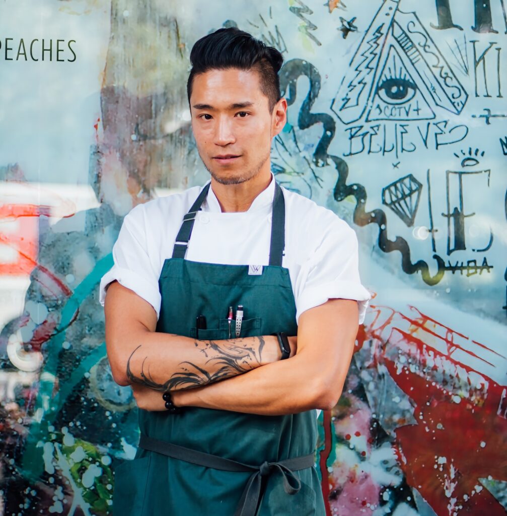 With a graffiti background, Chef Johnson Wu poses in his kitchen uniform.